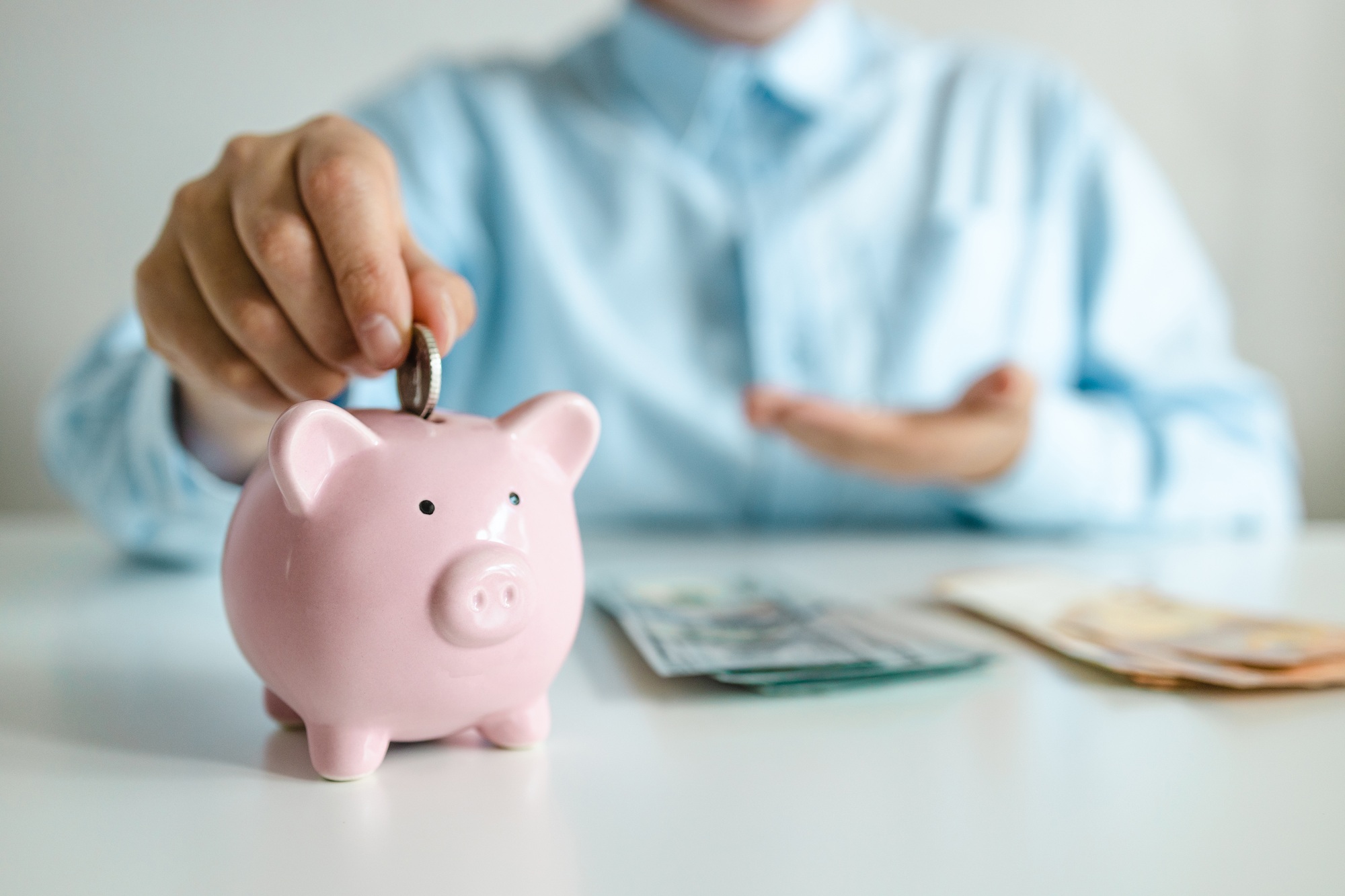 Depositing money in a piggy bank on wooden table at home